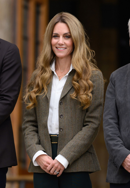 Kate Middleton appears at an event with long honeyblonde hair. She wears a white shirt and jacket.